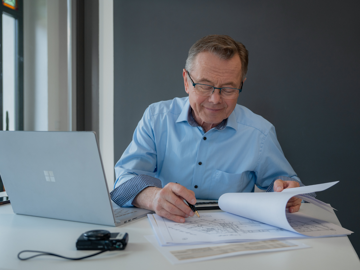 Zertifizierter Sachverständiger Hans-Jürgen Reppe kontrolliert Grundrisspläne am Schreibtisch.